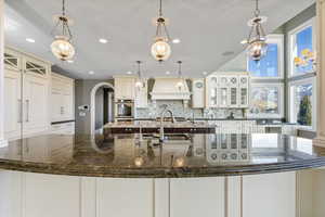 Kitchen featuring arched walkways, backsplash, custom exhaust hood, and recessed lighting