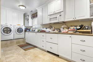 Laundry area with independent washer and dryer, light tile patterned flooring, cabinet space, a sink, and visible vents