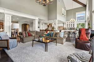 Living area featuring decorative columns, a chandelier, high vaulted ceiling, and dark wood-style floors