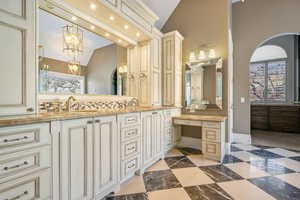 Full bath with double vanity, a sink, baseboards, and vaulted ceiling