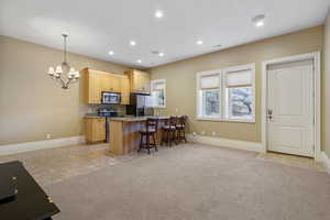 Kitchen with baseboards, appliances with stainless steel finishes, a breakfast bar, and an inviting chandelier