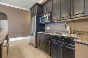 Kitchen featuring appliances with stainless steel finishes, arched walkways, a sink, stone counters, and ornamental molding