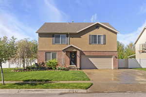 Traditional home with concrete driveway, brick siding, an attached garage, and fence