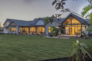 Rear view of house with a lawn, a standing seam roof, metal roof, and stone siding