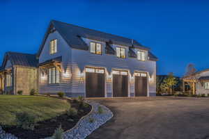 View of front of house with a standing seam roof, driveway, metal roof, a garage, and a yard