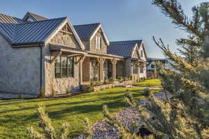 Back of house with a standing seam roof, a lawn, metal roof, and stone siding