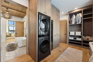 Laundry room with light wood-style floors, stacked washing maching and dryer, and wooden ceiling