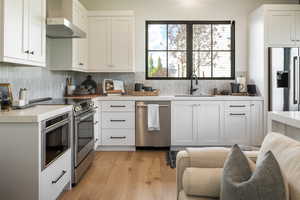 Kitchen with light countertops, wall chimney exhaust hood, a sink, light wood-style flooring, and stainless steel appliances