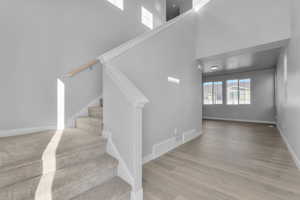 Stairs with baseboards, a high ceiling, visible vents, and wood finished floors