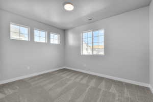Carpeted spare room featuring visible vents, a textured ceiling, and baseboards