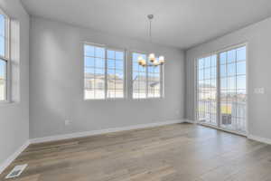 Empty room featuring a notable chandelier, visible vents, baseboards, and light wood finished floors