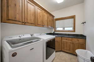 Laundry room with cabinet space, a sink, light tile patterned floors, and washing machine and dryer included.