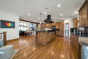Kitchen with a kitchen island, light wood-style floors, a breakfast bar area, brown cabinets, and island exhaust hood