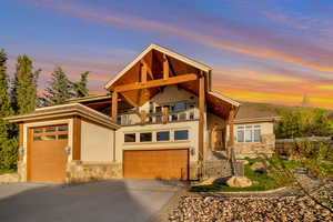 View of front of property with driveway, a balcony, stone siding, and stucco siding