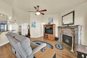 Living room featuring ceiling fan, a fireplace, baseboards, high vaulted ceiling, and light wood-style floors