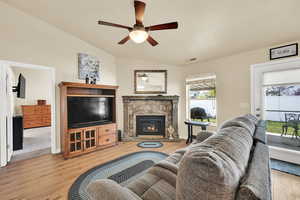 Living area featuring ceiling fan, a fireplace, wood finished floors, vaulted ceiling, and visible vents