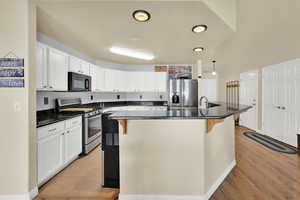 Kitchen featuring light wood-style floors, a breakfast bar area, stainless steel appliances, white cabinetry, and a center island with sink