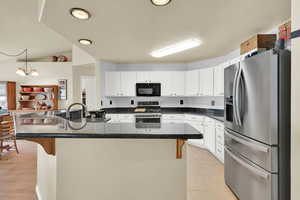 Kitchen featuring a breakfast bar, a center island with sink, stainless steel appliances, white cabinetry, and pendant lighting