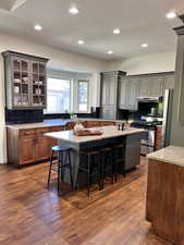 Kitchen featuring an island with sink, a kitchen bar, under cabinet range hood, backsplash, and stainless steel appliances
