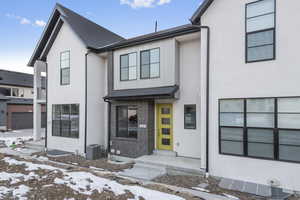 View of front facade featuring brick siding, central AC unit, stucco siding, and a shingled roof