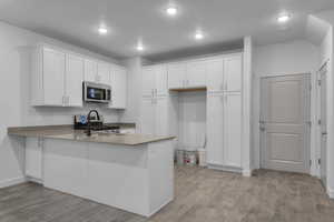 Kitchen with white cabinets, light wood-type flooring, stainless steel appliances, and a peninsula