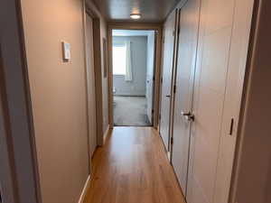 Corridor with baseboards, a textured ceiling, and light wood finished floors