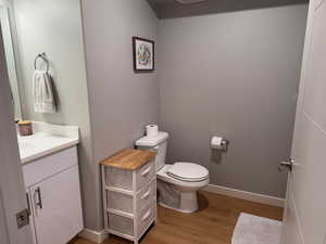 Bathroom featuring toilet, vanity, wood finished floors, and baseboards