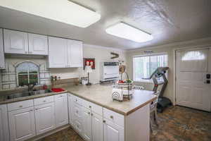 Kitchen with white cabinets, a sink, a peninsula, ornamental molding, and stone tile flooring
