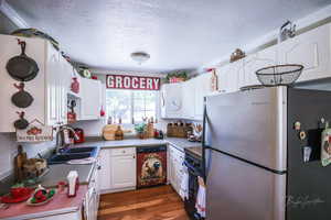 Kitchen with freestanding refrigerator, dishwashing machine, a textured ceiling, white cabinets, and a sink