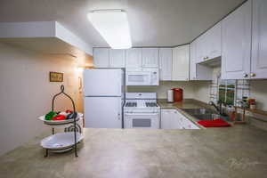 Kitchen with a sink, white cabinetry, a textured ceiling, and white appliances