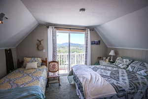 Bedroom with a textured ceiling, lofted ceiling, a mountain view, and access to exterior