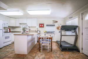 Kitchen with stone finish floor, ornamental molding, white appliances, and white cabinetry