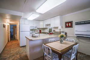 Kitchen with white cabinets, a sink, white appliances, a textured ceiling, and a peninsula