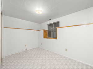 Carpeted spare room featuring baseboards, a textured ceiling, and visible vents