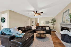 Living area with ceiling fan, a fireplace with raised hearth, wood finished floors, and stairs