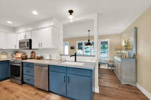 Kitchen featuring appliances with stainless steel finishes, blue & white cabinets, light wood finished floors, and a sink