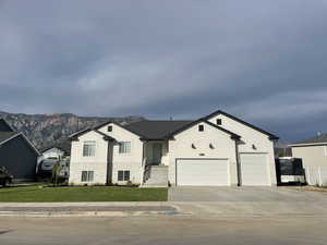 View of front facade featuring concrete driveway, a front yard, stucco siding, and a mountain view