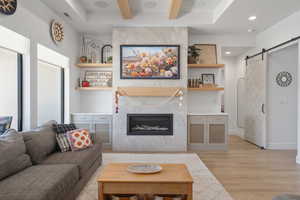 Living area featuring a barn door, beam ceiling, light wood finished floors, recessed lighting, and a high end fireplace
