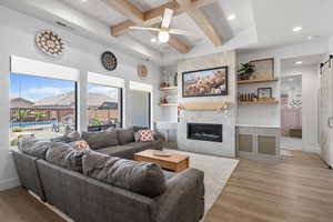 Living area featuring visible vents, a barn door, beam ceiling, light wood-style flooring, and a premium fireplace
