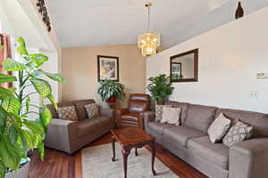 Living room with vaulted ceiling, wood finished floors, and a notable chandelier