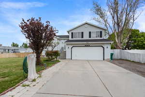Traditional-style home with concrete driveway, an attached garage, fence, and a front yard