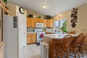 Kitchen featuring a breakfast bar area, a sink, light countertops, a peninsula, and white appliances