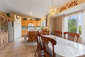 Dining room featuring light tile patterned floors, vaulted ceiling, and a notable chandelier