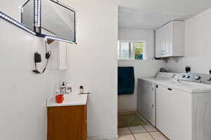 Clothes washing area with light tile patterned flooring, a textured ceiling, separate washer and dryer, a sink, and cabinet space