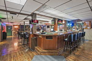 Bar featuring wooden walls, visible vents, a bar, and hardwood / wood-style flooring