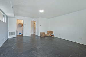 Interior space with a textured ceiling, visible vents, and concrete floors