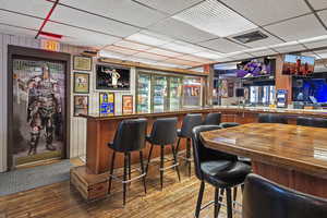 Bar with a bar, a paneled ceiling, visible vents, and hardwood / wood-style flooring