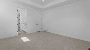 Unfurnished bedroom featuring visible vents, light carpet, baseboards, recessed lighting, and a tray ceiling