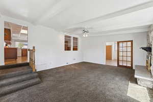 Unfurnished living room with stairs, carpet, ceiling fan, and beam ceiling