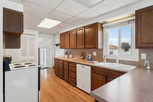 Kitchen with white appliances, a drop ceiling, light countertops, a sink, and light wood finished floors